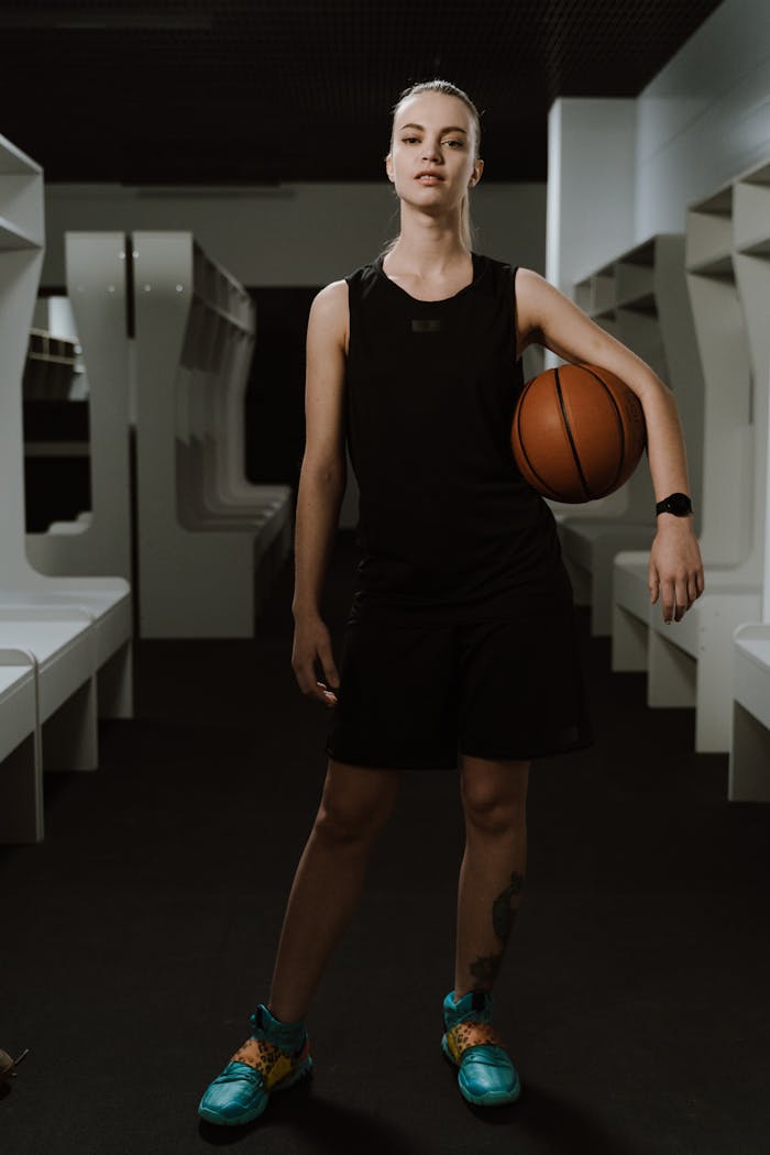 Young female athlete holding a basketball in a modern locker room setting.